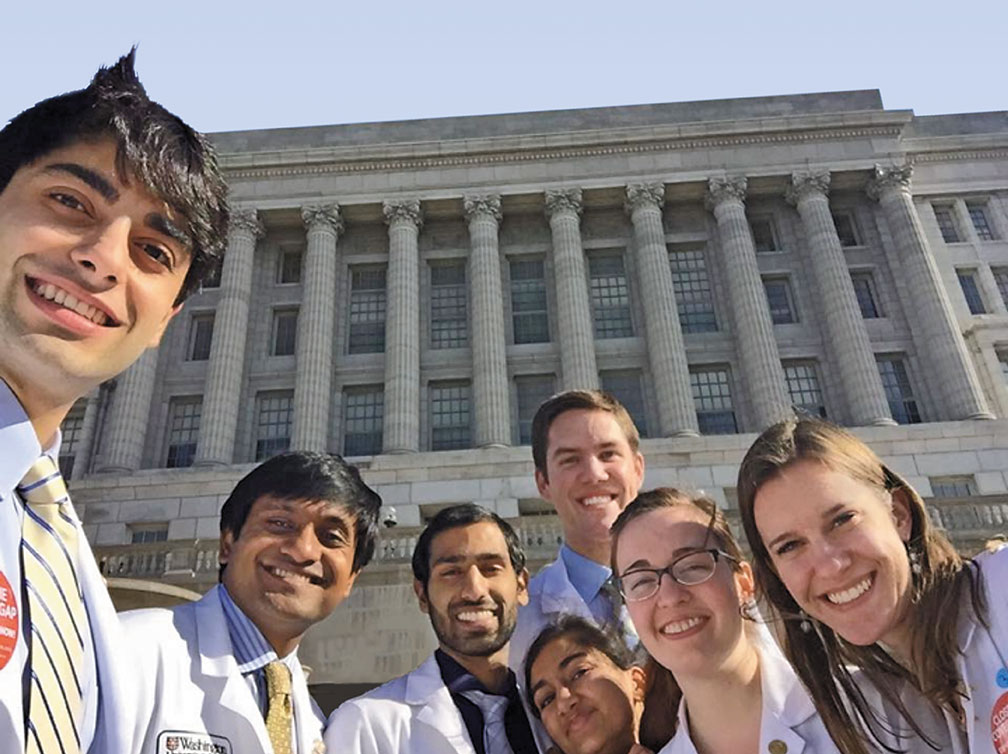 A group of six medical students standing in front of the Missouri state capitol building smiles into the camera